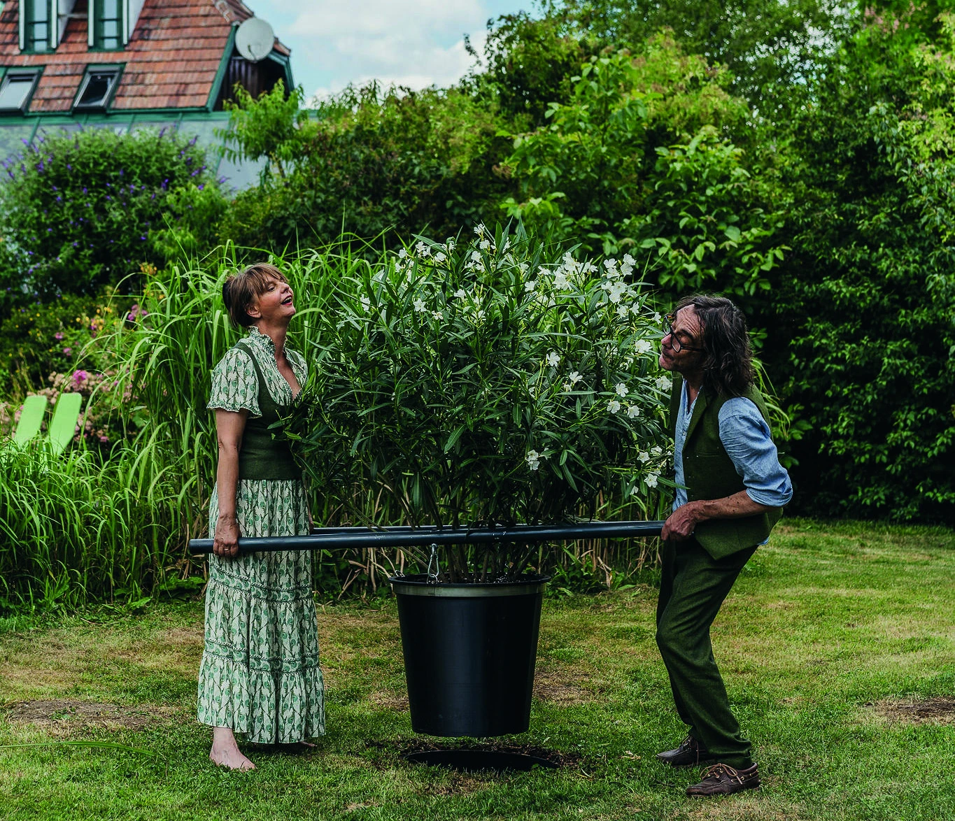 Zwei Personen heben den Olivia-FLEX-Pflanztopf mit Tragestangen aus dem Gartenboden.